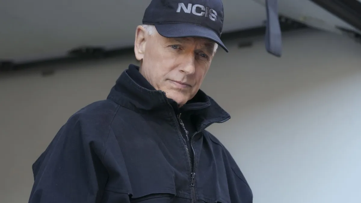 A character from NCIS is wearing a hat and looking down at something off-screen. 