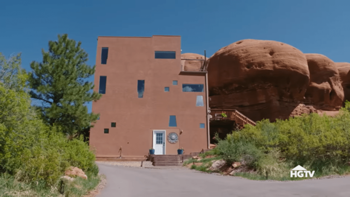 O exterior de um edifício simples empoleirado ao lado de uma enorme rocha vermelha. 