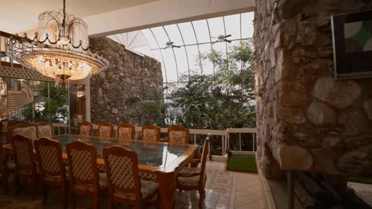 Uma sala de jantar com paredes de pedra e uma estufa semelhante a uma selva e um lustre espalhafatoso. 