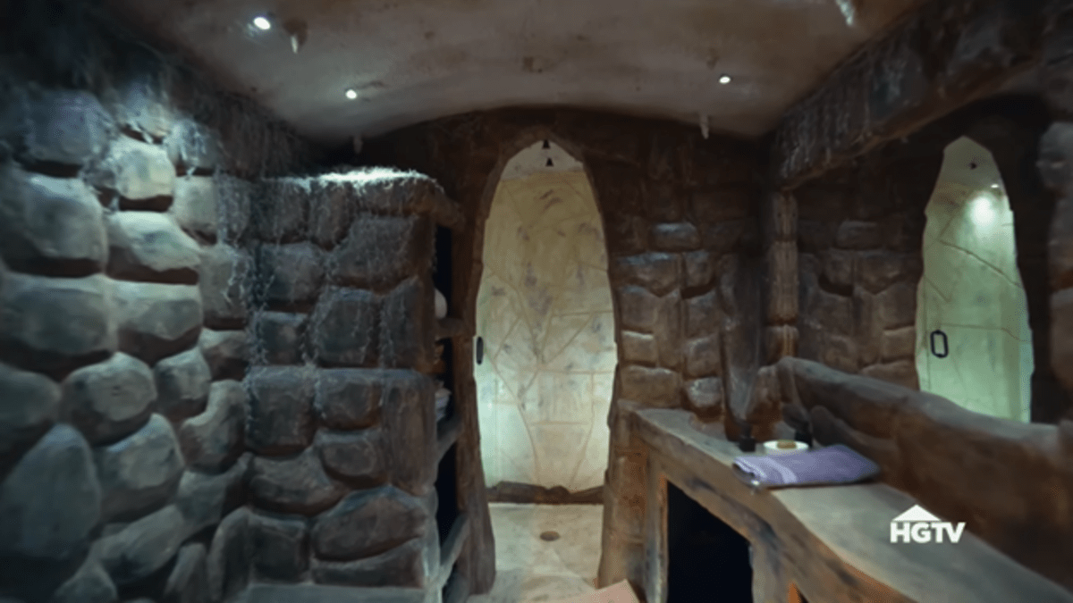 Uma caverna de pedra com um balcão de pedra falsa e armário de linho levando a um chuveiro para quatro pessoas. 