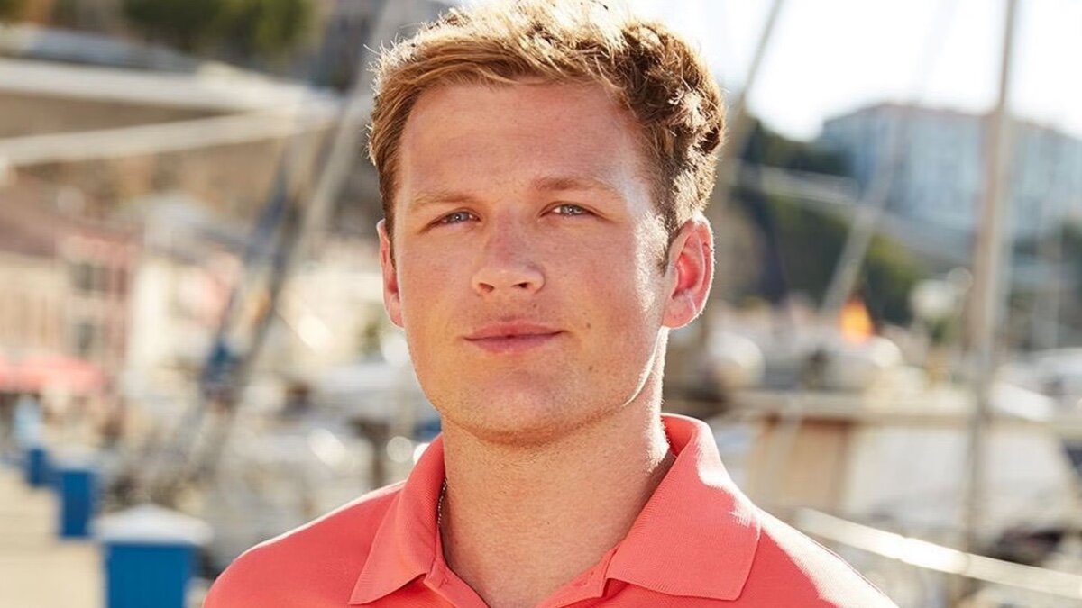 Tom Pearson smiles on boat in orange polo