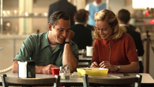 Lewis Pullman and Brie Larson as Calvin and Elizabeth Zott sitting next to each other at a cafeteria table smiling in Lessons in Chemistry on Apple TV