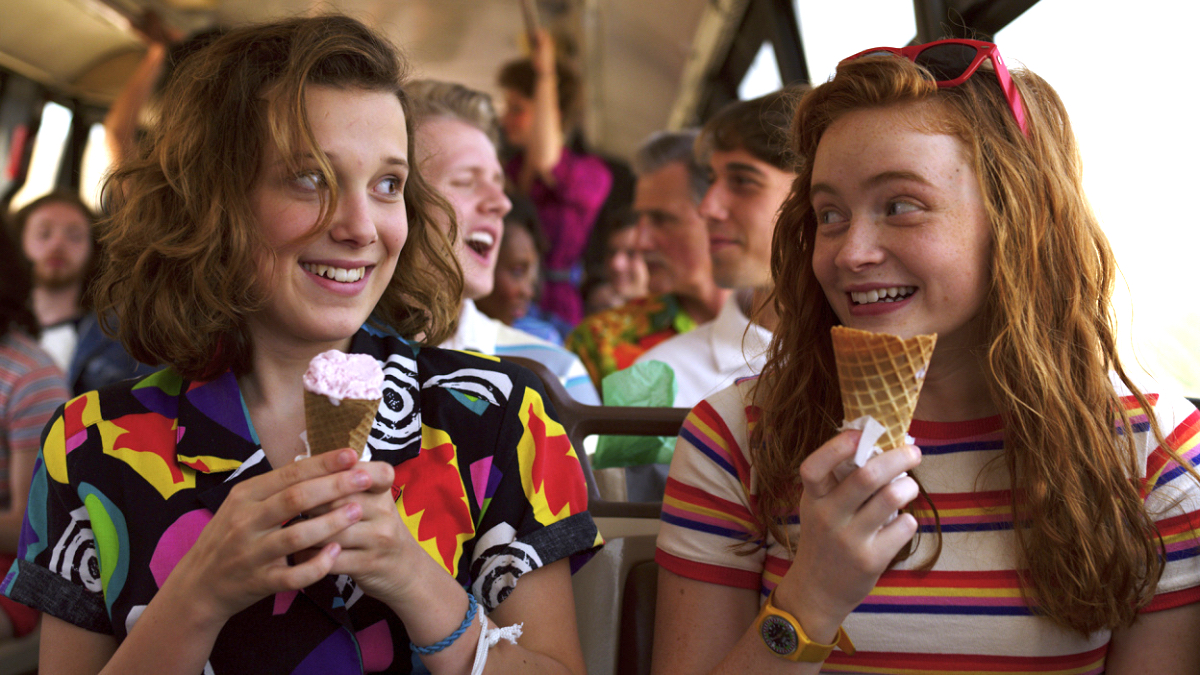 Millie Bobby Brown and Sadie Sink as Eleven and Max eating ice cream on a bus in Stranger Things season 3