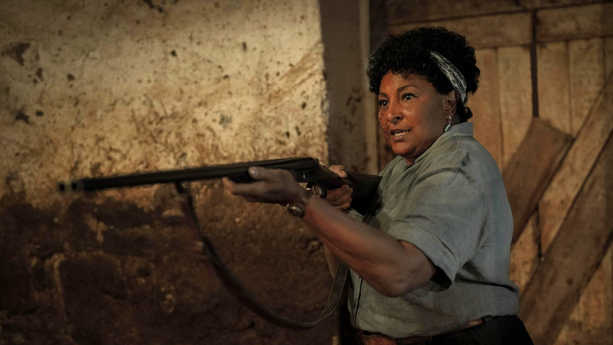 Marjorie (portrayed by Pam Grier) holding a gun to something off-screen.