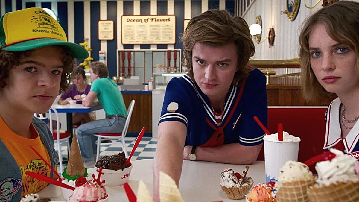 Os personagens de 'Stranger Things' Dustin (Gaten Matarazzo), Steve (Joe Keery) e Robin (Maya Hawke) olhando intimidadoramente para a câmera durante uma cena ambientada na sorveteria Scoops Ahoy da terceira temporada do programa.