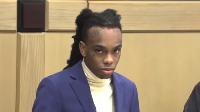 YNW Melly wearing a yellow turtle neck and blue blazer in a court room