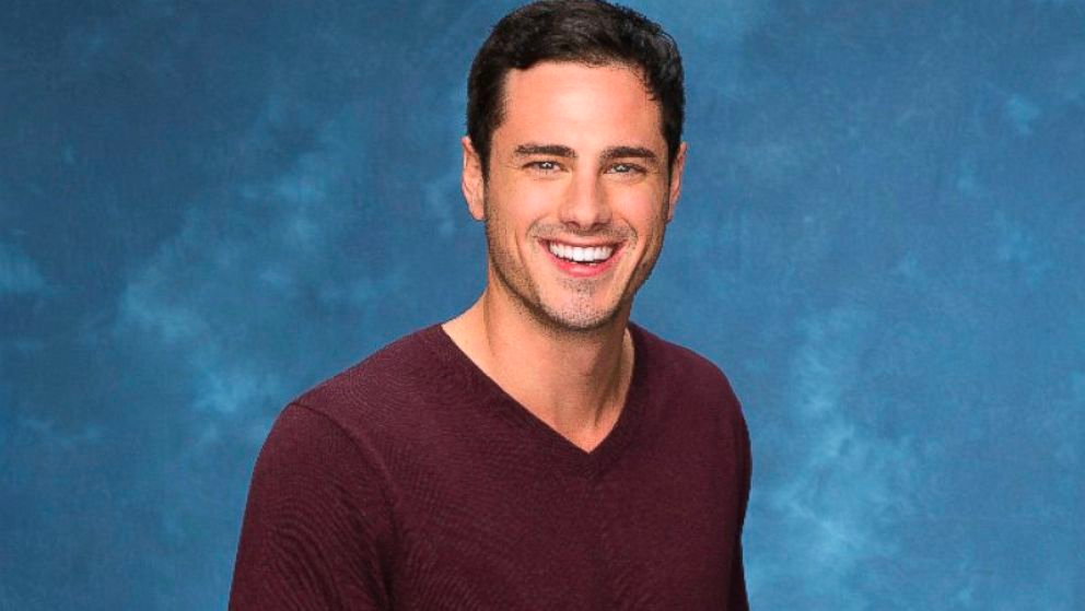 Ben Higgins smiles at the camera in front of a blue background.