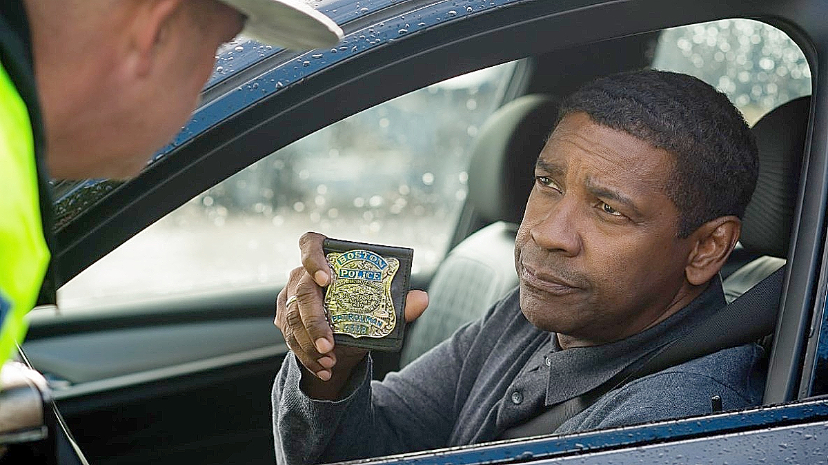 A character in The Equalizer is holding up a police badge in a car.
