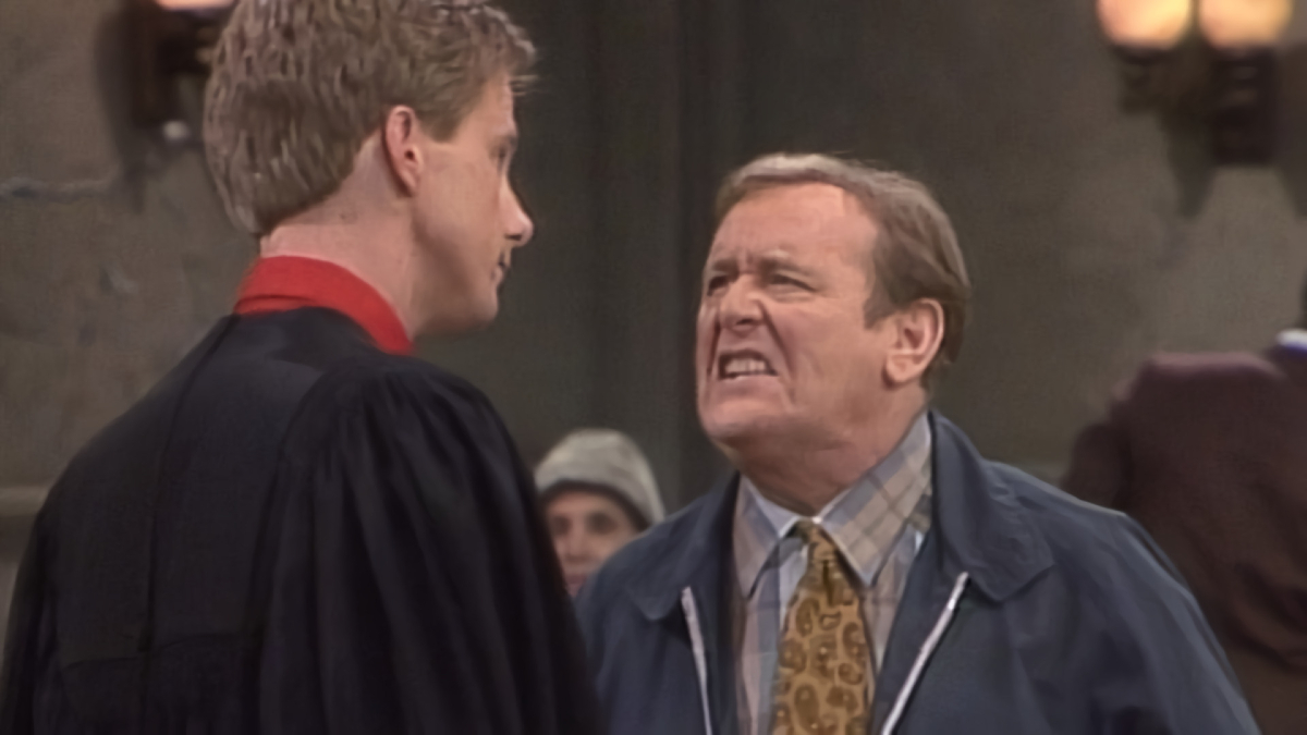 A man looks up angrily snaring at another man in judge robes who is much taller than him.