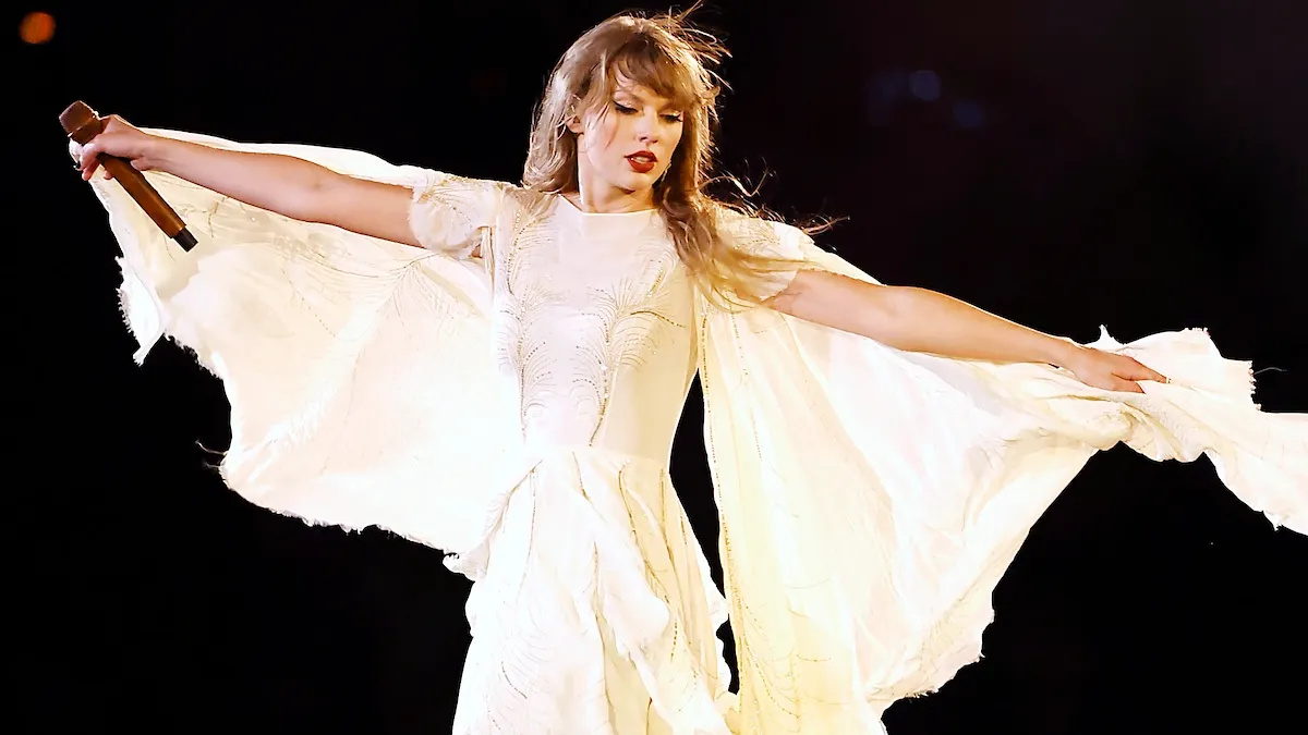 Taylor Swift wearing a flowy cream colored dress performing onstage during "Taylor Swift | The Eras Tour"
