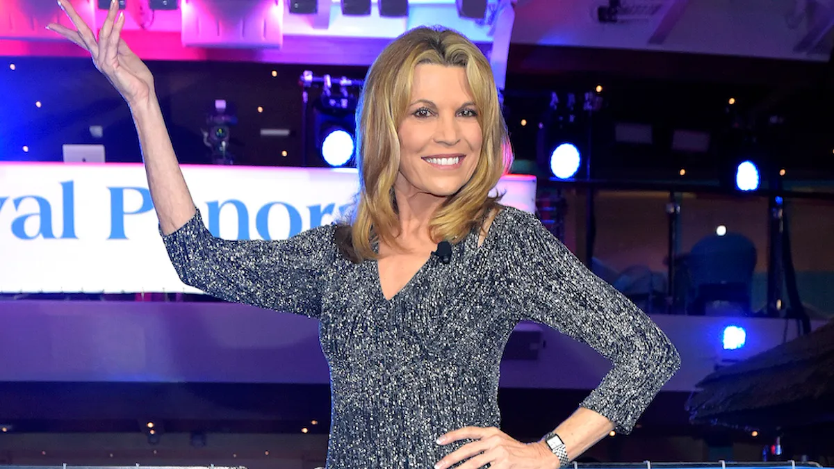 Vanna White in a sparkly dark silver dress with her signature hand raised