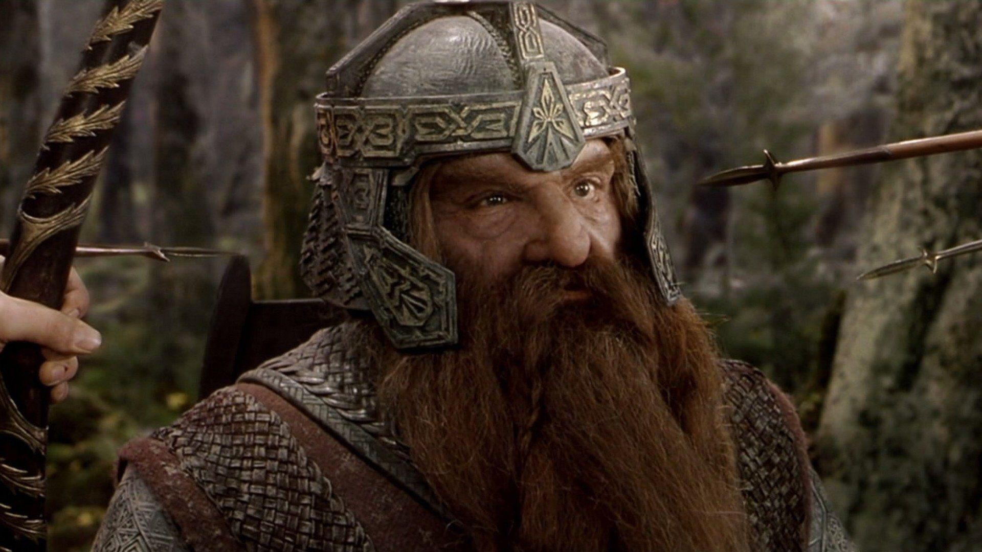 Gimli is waring a helmet and has weapons being held towards his head. 