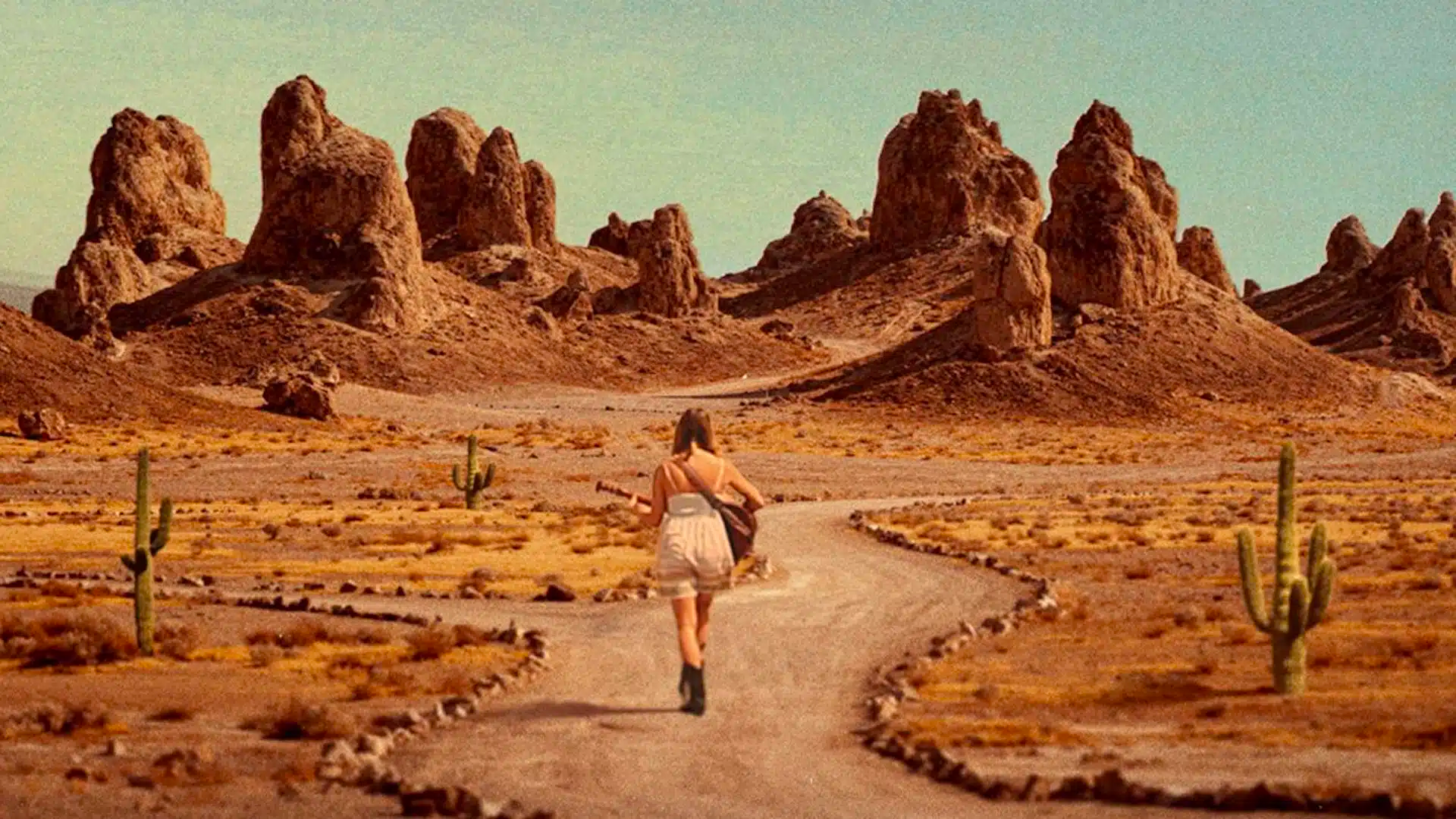 A woman is walking through a desert, holding a guitar, in The Outwaters. 