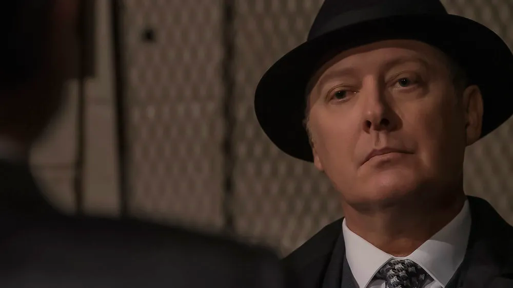 Red is wearing a hat and looking at something off camera in "The Blacklist". 