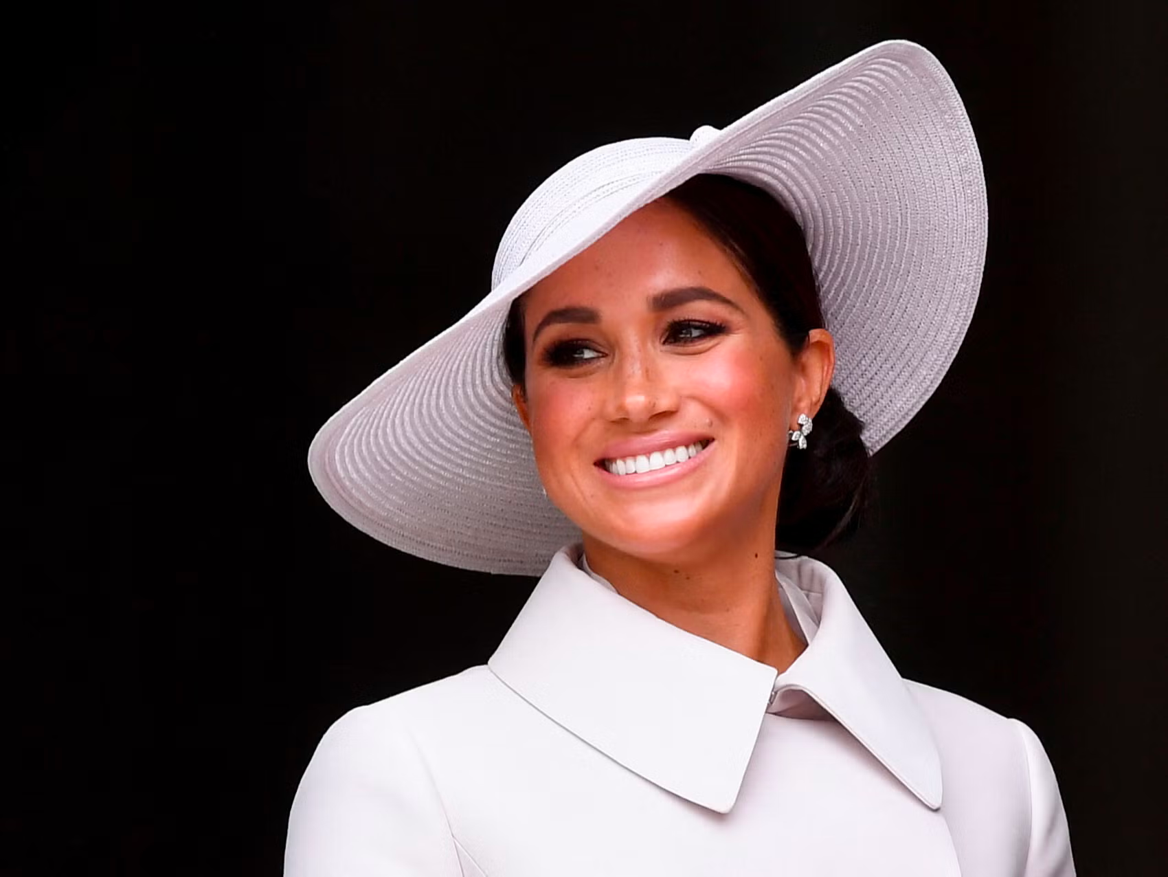 Meghan Markle is wearing a big hat and smiling.