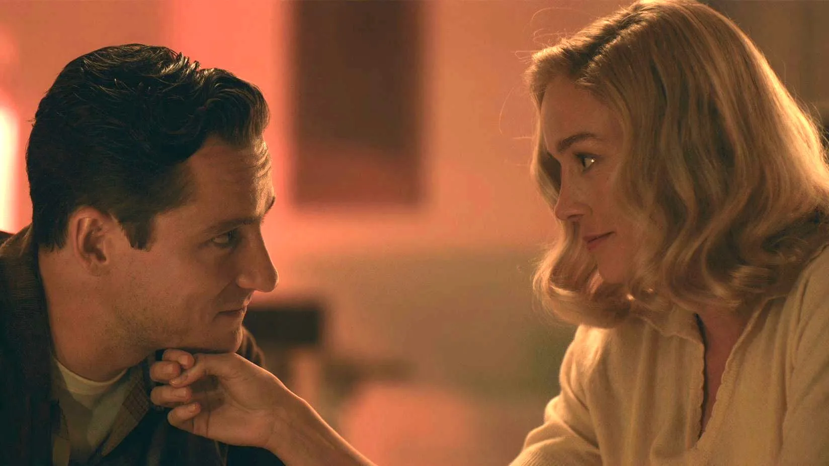 Calvin (Lewis Pullman) rests his chin on Elizabeth's (Brie Larson) hand as she stares him affectionately in 'Lessons in Chemistry'