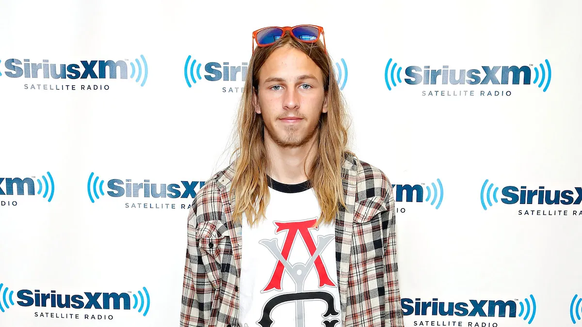 Riley Hawk wearing plaid over a T-shirt with sunglasses on his head in front of a Sirius XM step and repeat