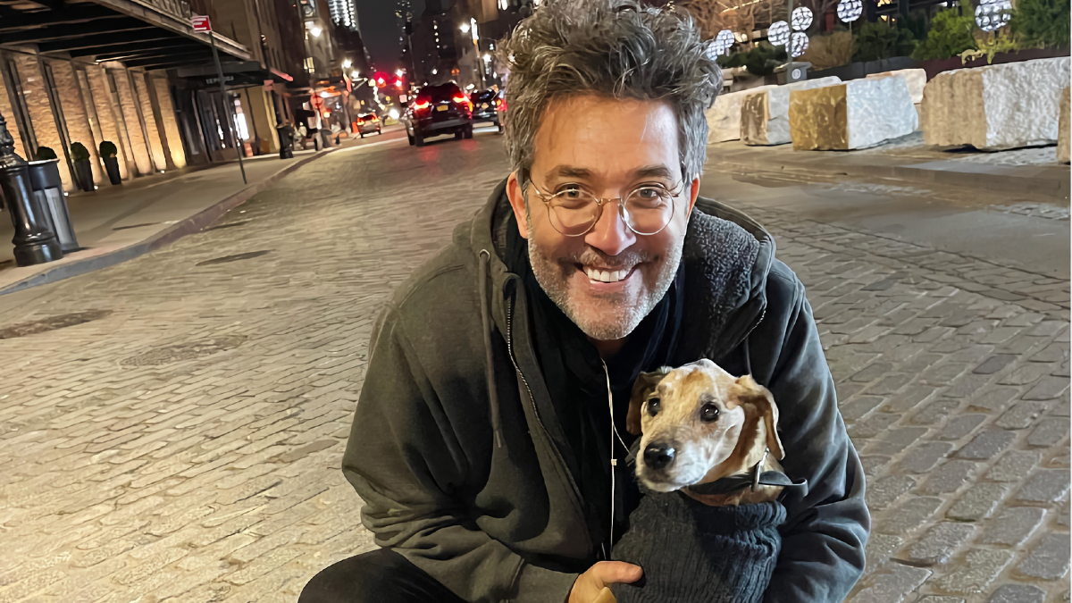 A man wearing a hoodie holds a dog wearing a sweater.