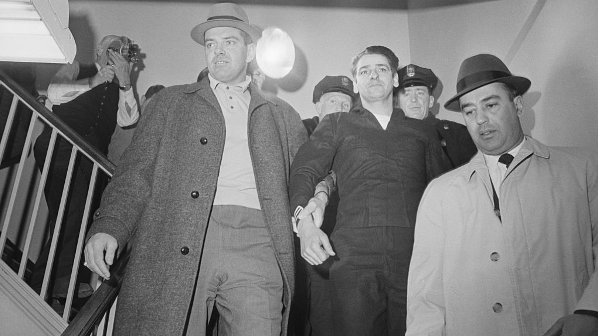 Confessed Boston Strangler Albert DeSalvo (c) is led from a press conference at the Lynn police station after his capture in a West Lynn uniform store. Wearing navy-type garb, DeSalvo said he "didn't bother anybody." His arrest came some 30 hours after his escape from Bridgewater State Hospital.