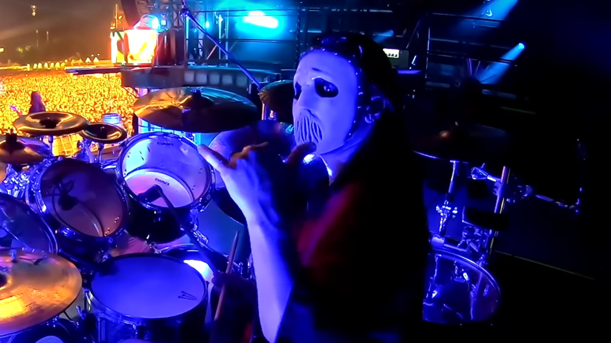 Jay Weinberg behind his drum set, flashing a hang loose sign.