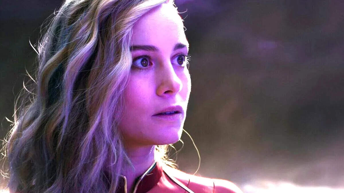 A close-up shot of a wide-eyed Captain Marvel (Brie Larson) as her face is bathed in a purple glow in The Marvels.