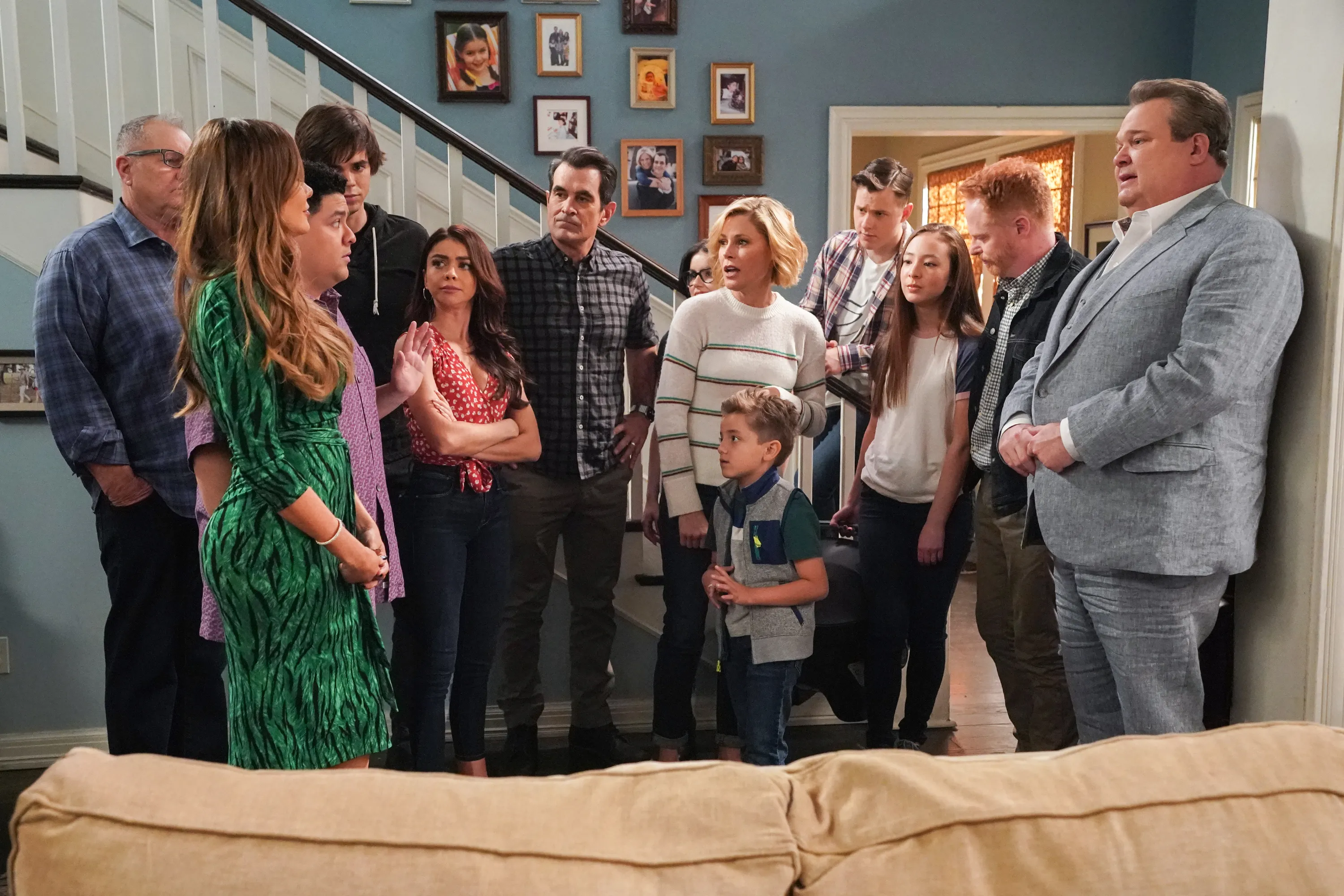 The entire Modern Family cast is gathered around in a living room. 