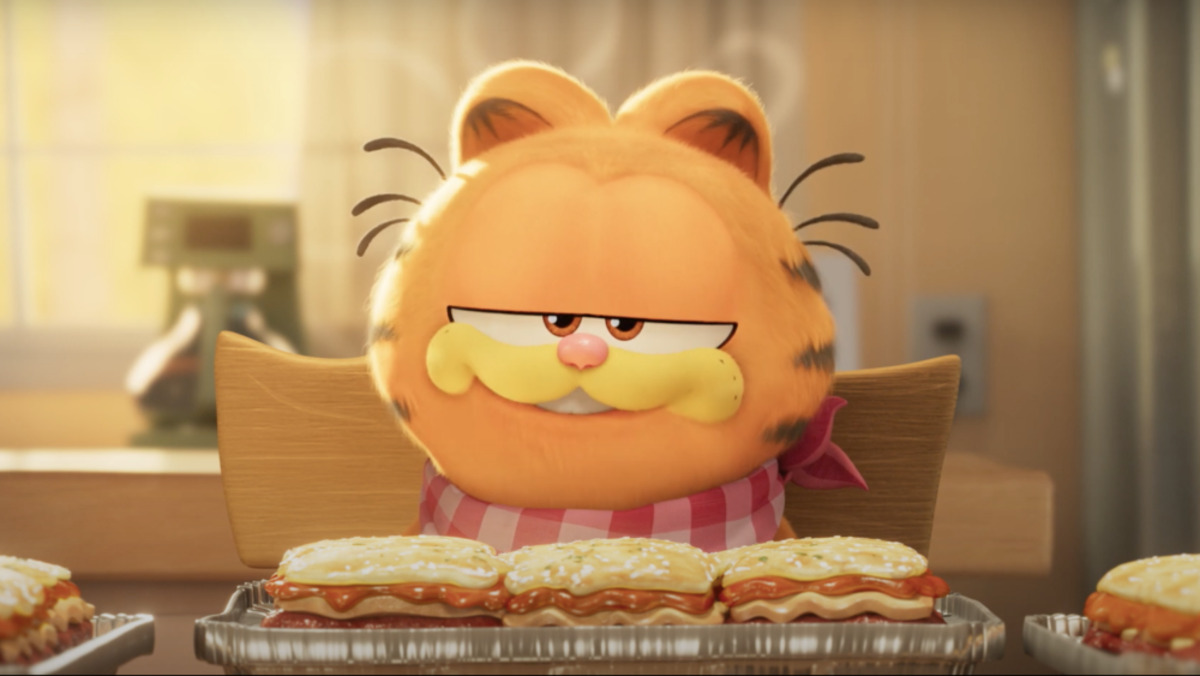 Garfield grins at the camera in front of a heaped plate of lasagna in a still from 'The Garfield Movie'
