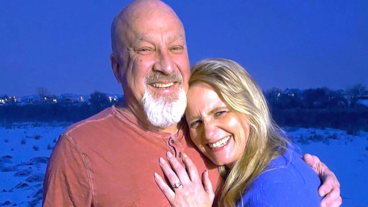 Christine Brown and David Woolley posing together outside, with Christine showing off her engagement ring on her hand, pressed against David's chest