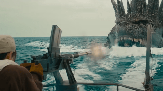 Godzilla swimming toward a boat firing a machine gun at him.
