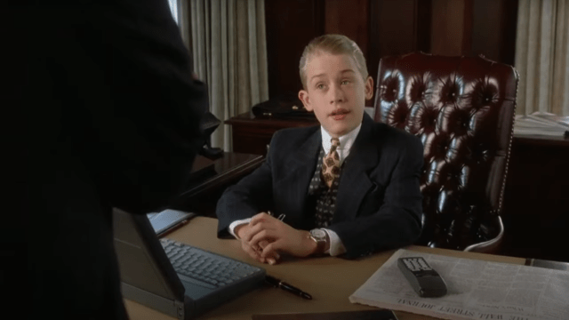 Macaulay Culkin as Richie Rich, sitting at a desk with the Wall Street Journal