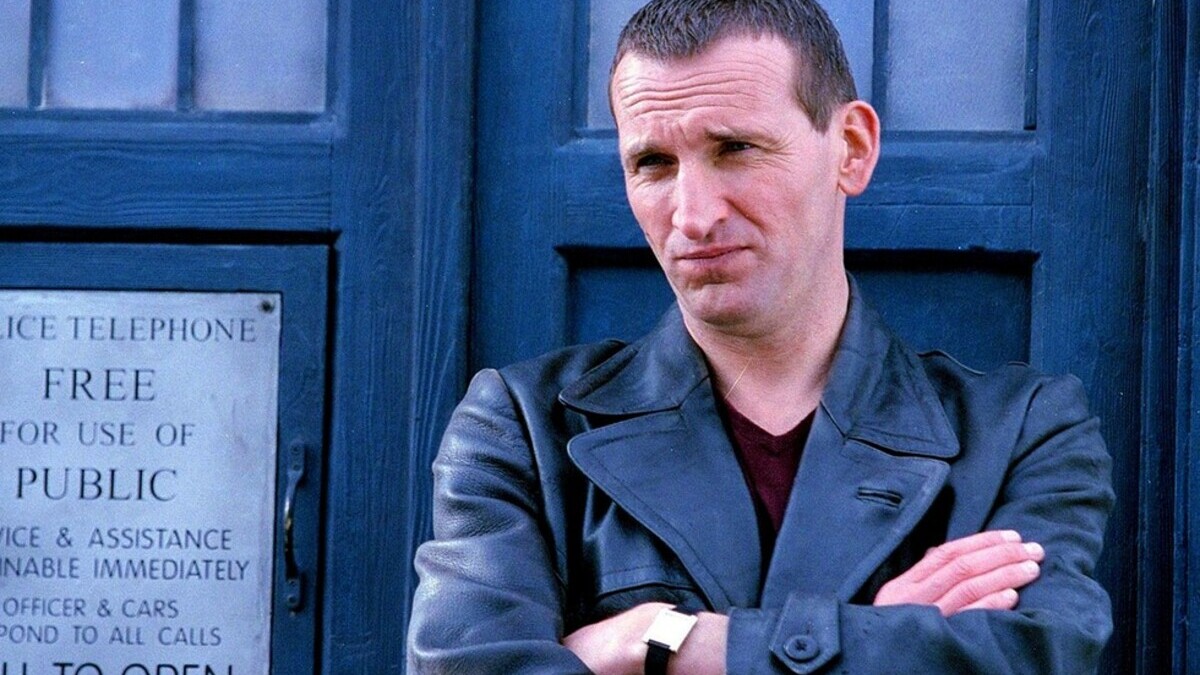 Christopher Eccleston's Ninth Doctor strands with his arms folded in front of the TARDIS.