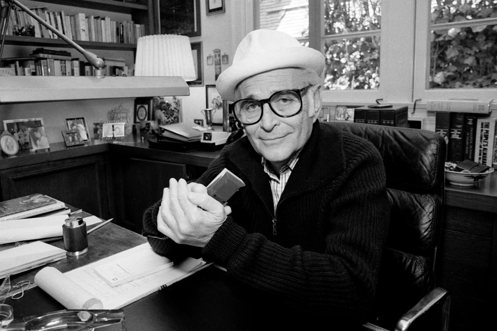 Norman Lear is shown sitting at his desk in a black and white photo. 