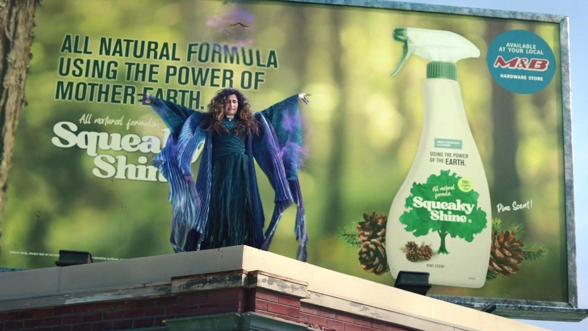 Agatha Harkness (Kathryn Hahn) stands in front of a billboard on a rooftop with her arms spread in the WandaVision series finale.