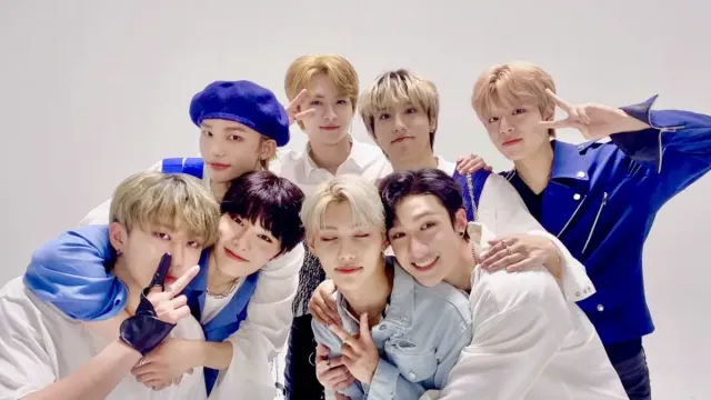 The members of the K-pop group Stray Kids are all wearing smiles as they pose for a cute group photo.