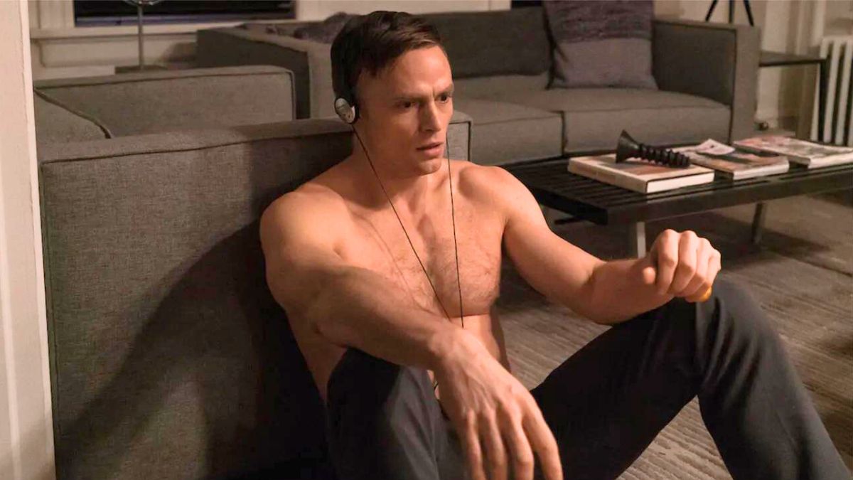 A shirtless Benjamin Pointdexter (Wilson Bethel) listens to headphones while leaning against a chair in his apartment in Daredevil season 3