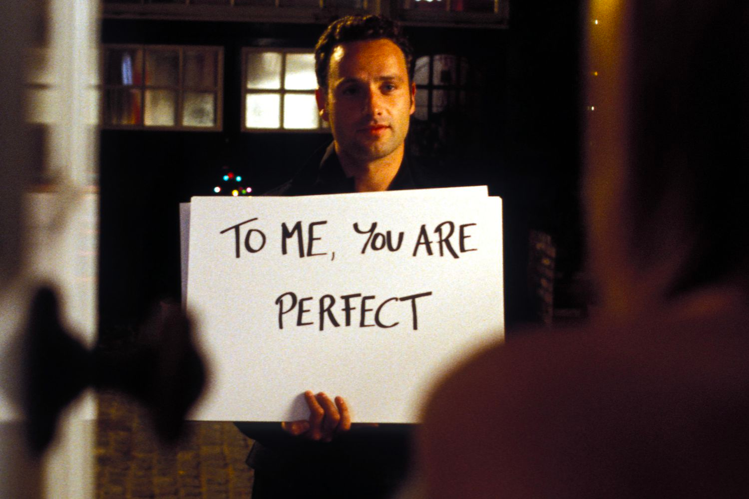 A character is holding a sign that says "To Me, You Are Perfect" in Love Actually.