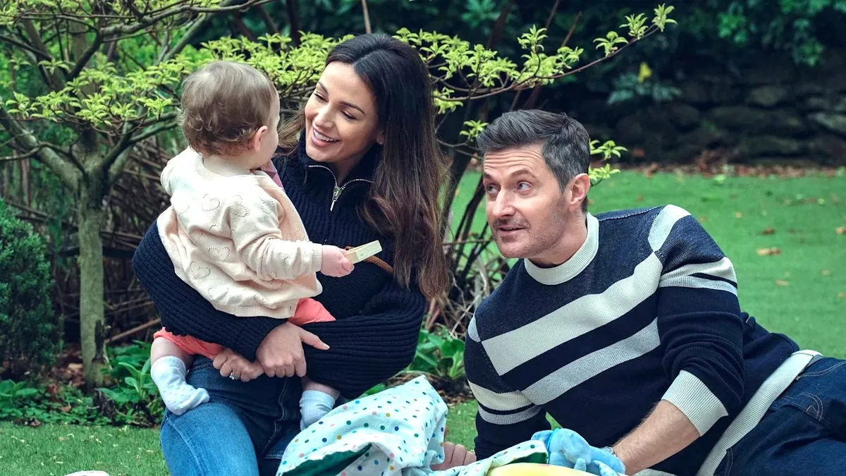 Maya (Michelle Keegan) and Joe Burkett (Richard Armitage) smile and play with their young daughter Lily in Netflix's Fool Me Once. 