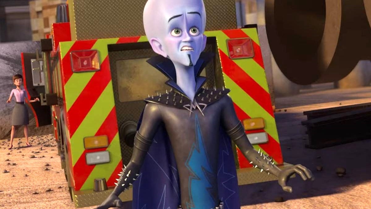 Megamind, with Roxanne Ritchi in the background, stands in front of an ambulance with a look of shock on his face