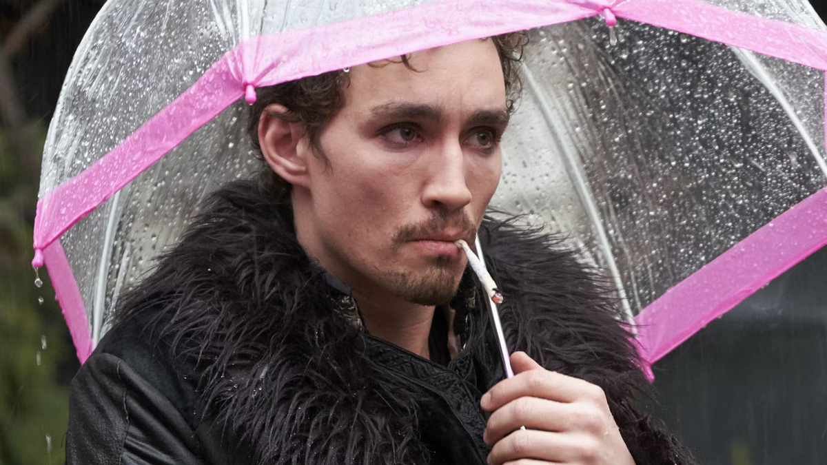 Klaus Hargreeves smoking a cigarette under a pink umbrella in season 1 of Netflix's The Umbrella Academy.