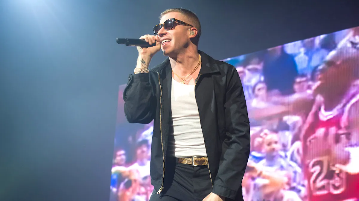Macklemore wearing a black jacket, white undershirt, and dark sunglasses during a performance at Le Zenith in Paris, France