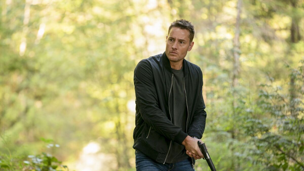 Justin Hartley as Colter Shaw trails through the woods with a gun in Tracker