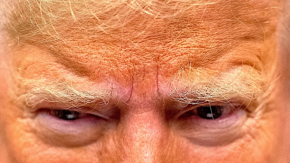 A close-up of Donald Trump's angry eyebrows and chalky, orange-makeup face