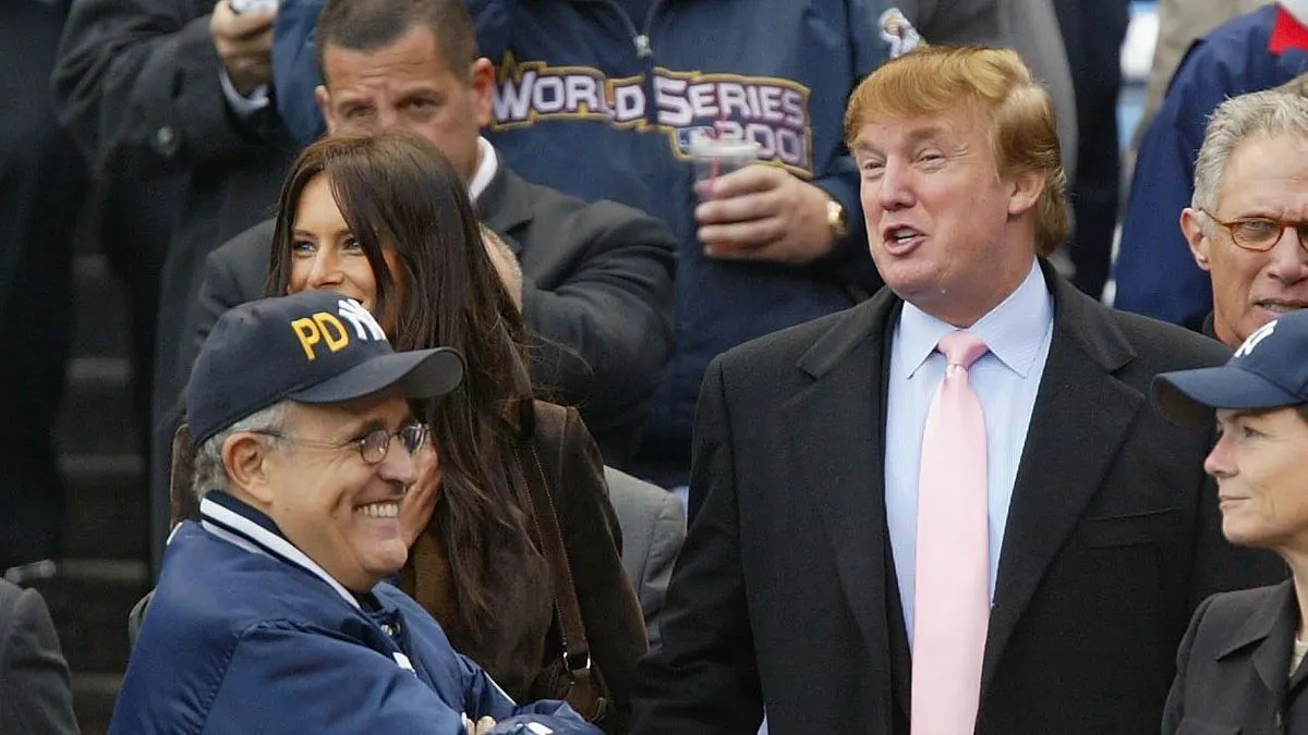 Real estate magnate Donald Trump talks with former New York City mayor Rudy Giuliani while current mayor Michael Bloomberg (far R) eats popcorn before the start of game 6 of the American League Championship Series between the Yankees and Boston Red Sox on October 15, 2003 at Yankee Stadium in the Bronx, New York. (Photo by Ezra Shaw/Getty Images)