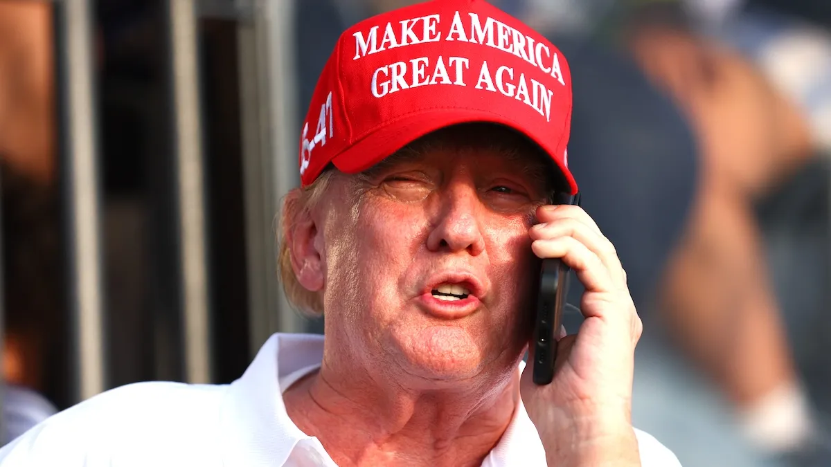 Donald Trump in a red MAGA hat and a white polo doing nothing important while talking into a cell phone