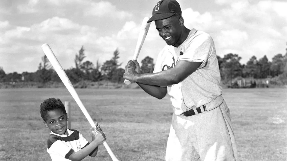 Jackie Robinson, (1919-1972), the baseball star, is shown here teaching his son Jackie Jr. how to bat.