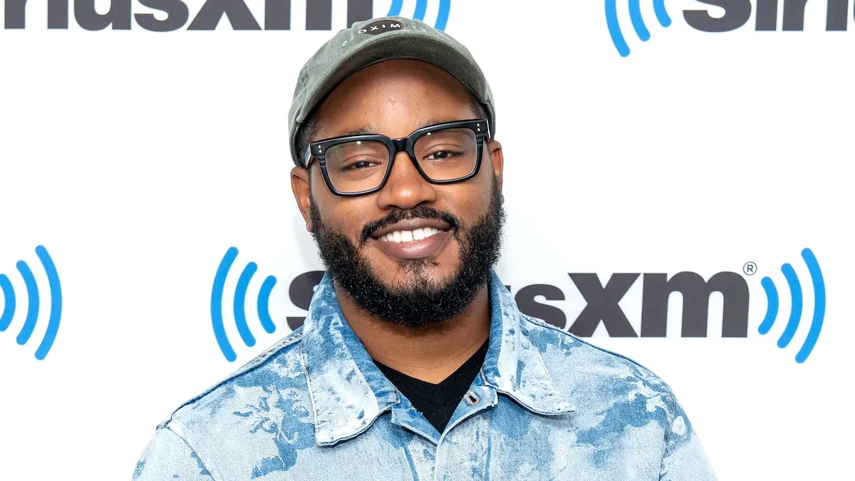 Ryan Coogler in black glasses, a hat, and a white and blue jean shirt visiting SiriusXM at SiriusXM Studios on June 12, 2023 in New York City.