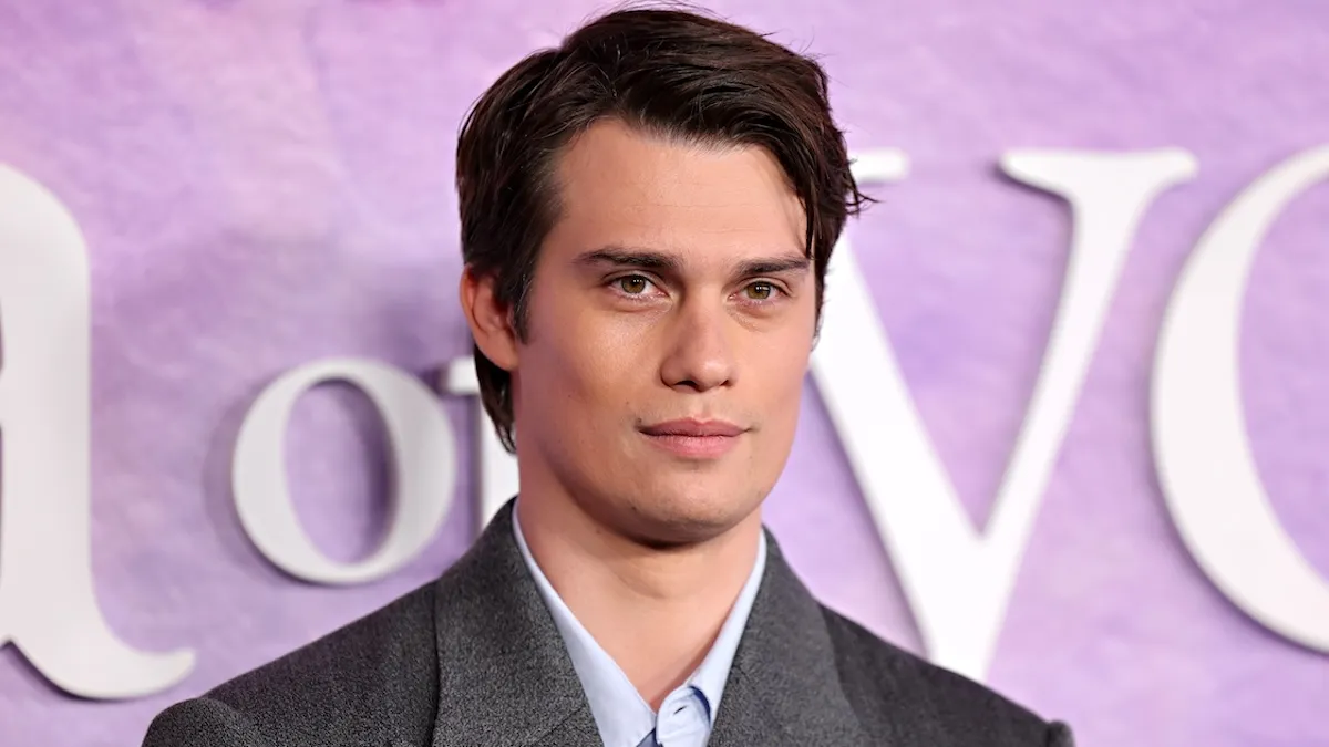 Nicholas Galitzine standing in front of a pink backdrop dressed in a grey suit on the red carpet of Prime Video's "The Idea Of You"