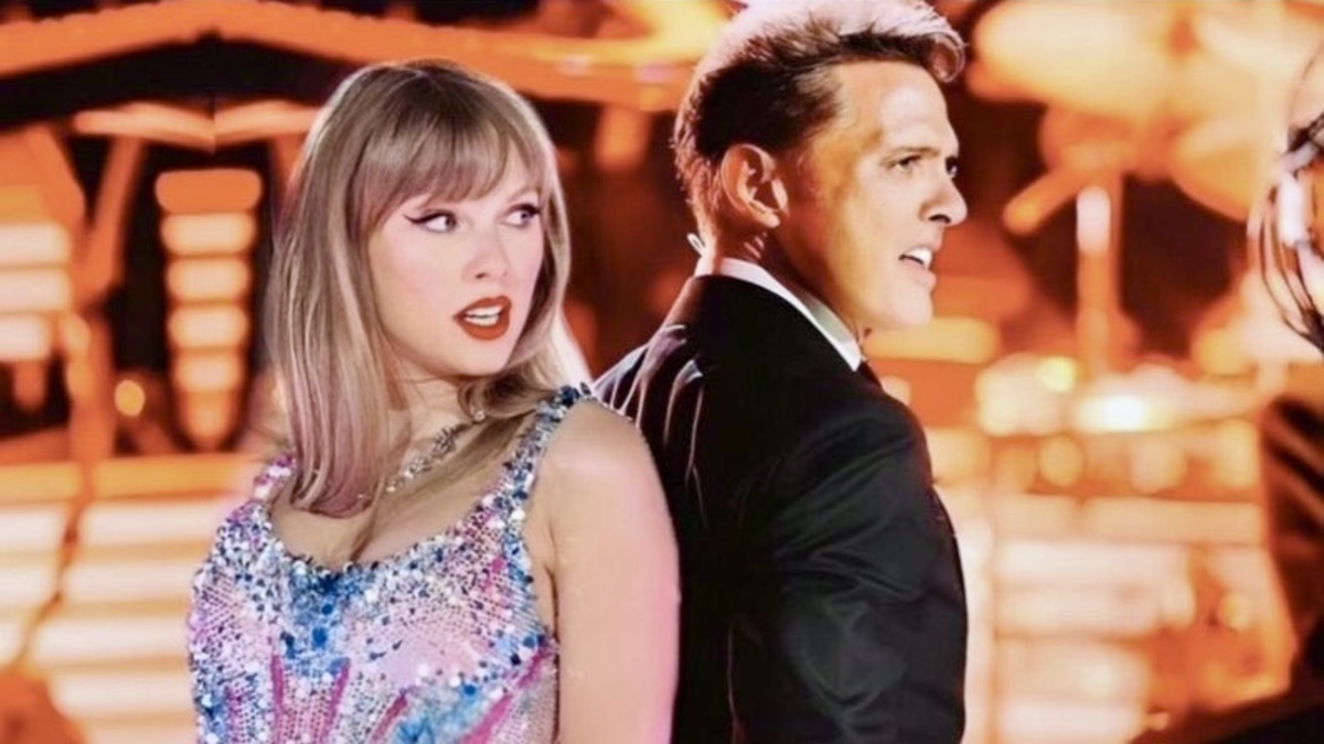 An edited photo of Taylor Swift and Luis Miguel standing back-to-back on stage, and staring intensely at the audience