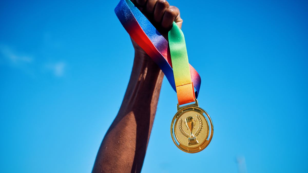 Raised hand holding a gold medal against blue sky. Victory and achievement concept.