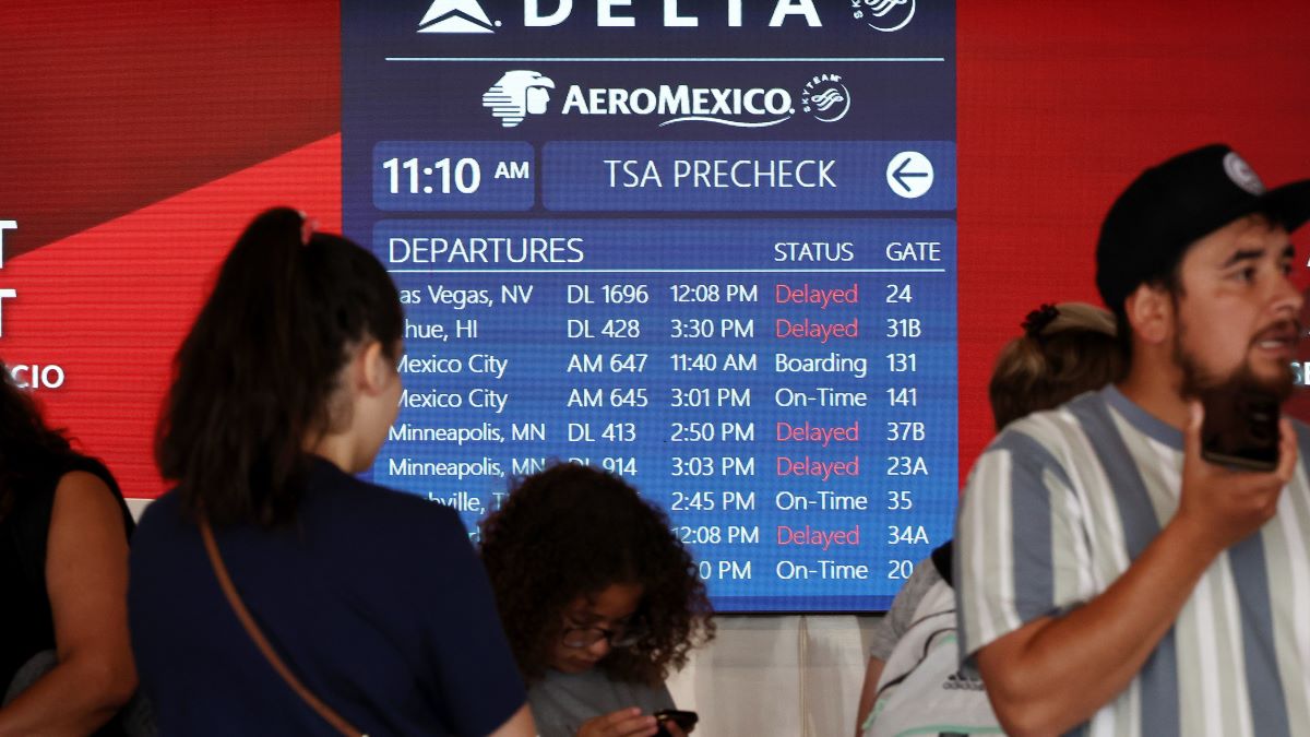 Travelers wait in line, as a flight board shows delays, on the check-in floor of the Delta Air Lines terminal at Los Angeles International Airport (LAX) on July 23, 2024 in Los Angeles, California. Delta Air Lines is still reeling in the aftermath of the CrowdStrike outage with 24 flights cancelled and 27 flights delayed at LAX today and 434 cancelled Delta flights nationwide today. (Photo by Mario Tama/Getty Images)